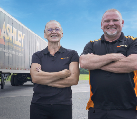 Ashley drivers smiling and crossing their arms next to an Ashley Semitruck