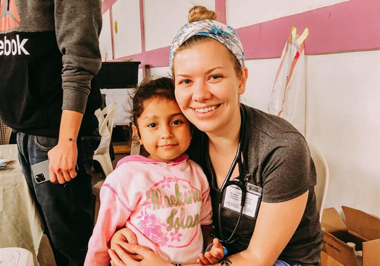 A female nurse is smiling and holding a young girl in her arms