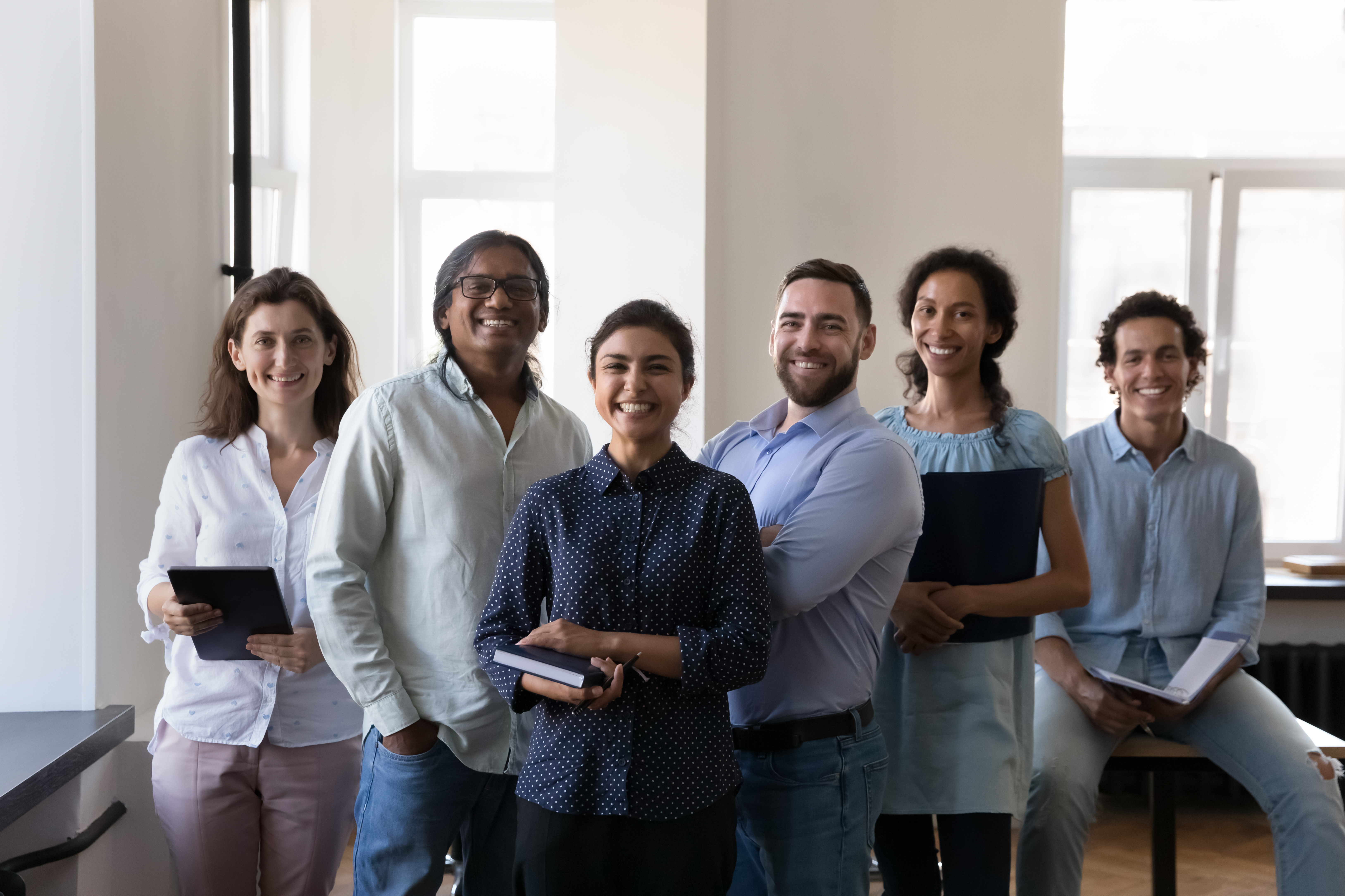 A group of people are smiling and looking at the camera while holding notepads