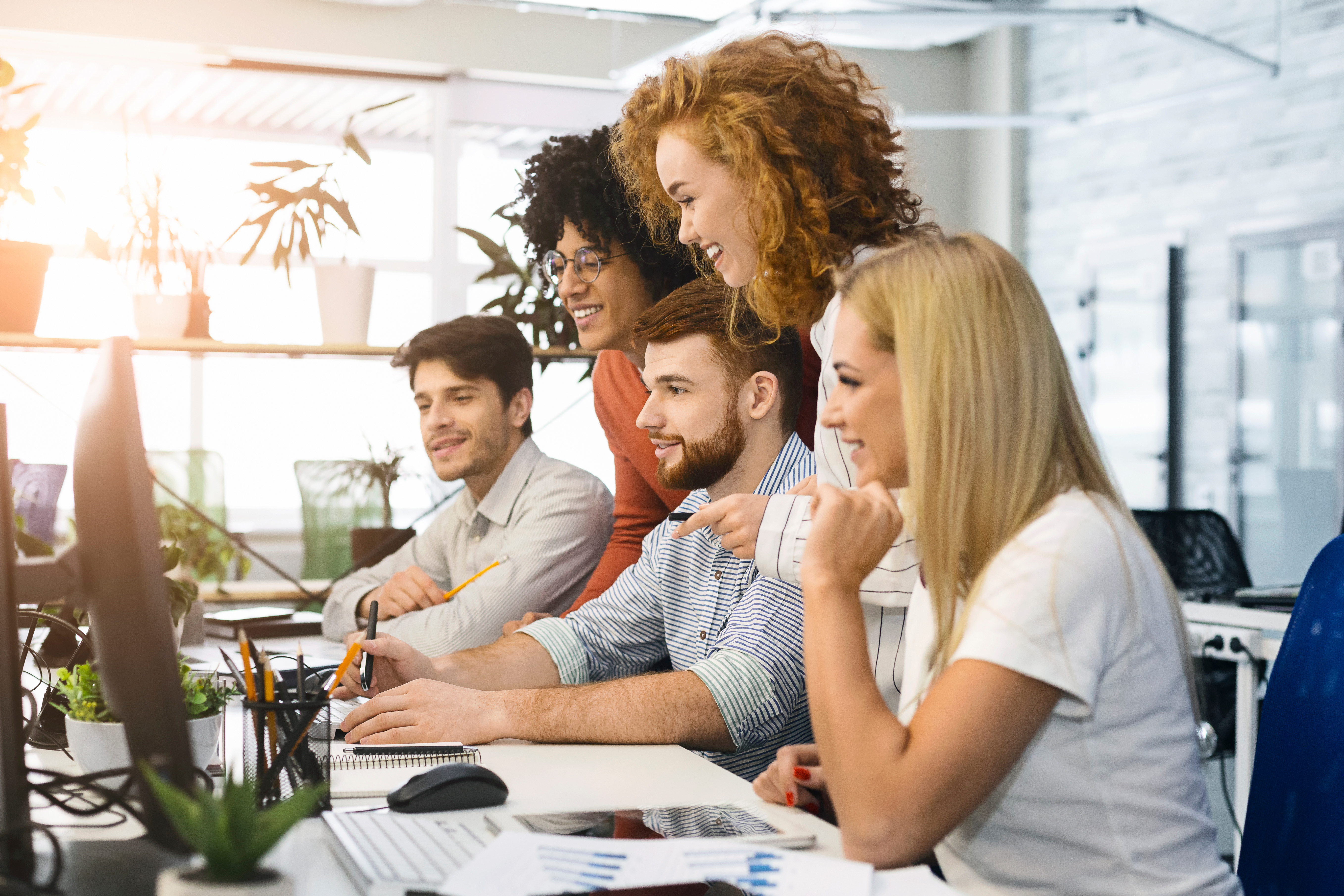 A group of smiling employees are looking at 2 computer screens