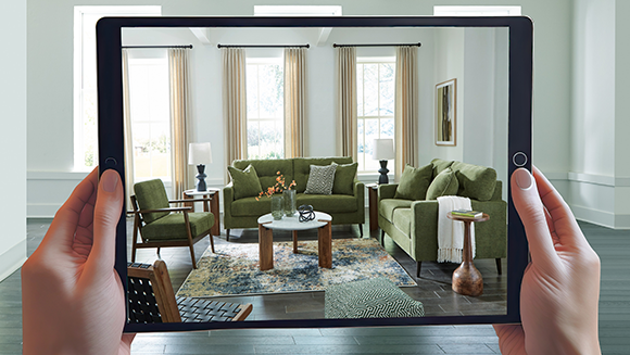 Two hands holding an iPad which visualize a couch with decor in the screen