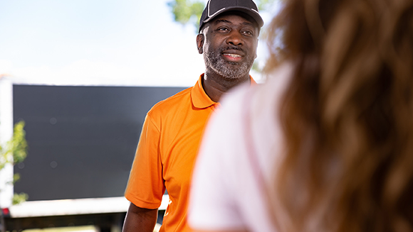 Ashley Driver with orange shirt is greeting a lady