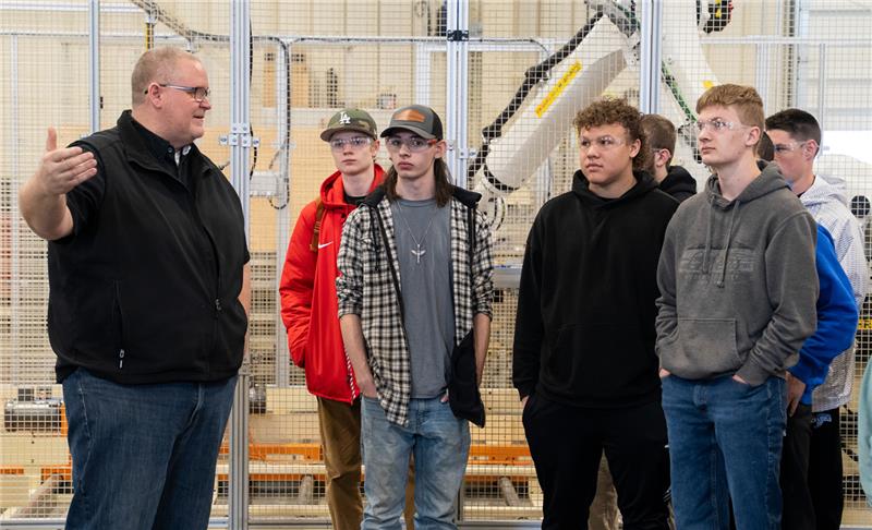 A group of young kids are in a tour of the facility , with an Ashley associate talking to them.